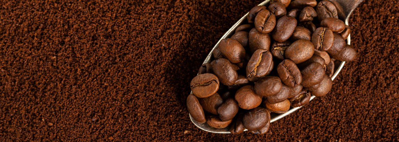 Coffee beans on spoon on ground coffee background. Closeup.